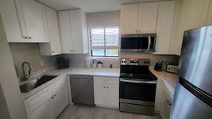 A compact kitchen with white cabinets, a stainless steel refrigerator, a microwave, a stove, and a dishwasher.