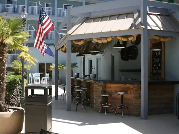 An outdoor bar area with a rustic wooden counter, stools, and an American flag.
