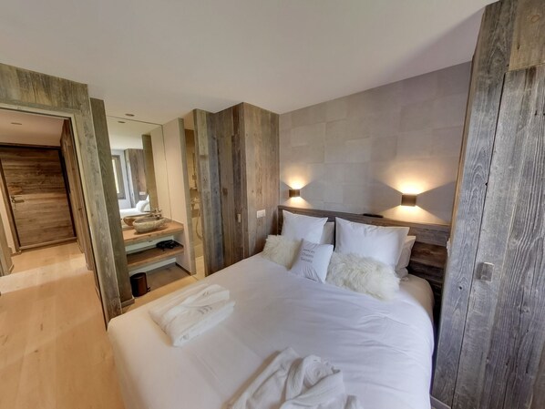 A bedroom with a large bed, wooden headboard, two wall-mounted lights, a wooden door, and a mirror.