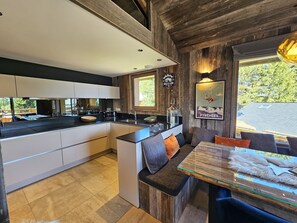 Cozinha moderna com ilha central, área de jantar com mesa de vidro e vista para o exterior.