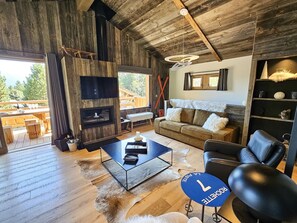 A rustic cabin interior with a wooden ceiling, a fireplace, a sofa, a coffee table, and a television.