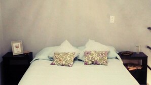 A neatly made bed with a white bedspread and two floral pillows, flanked by black nightstands with a framed picture and a glass of water. - Loft " El Mestizo" (Celestún)