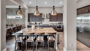 Una cocina moderna con una isla grande, armarios de madera oscura, electrodomésticos de acero inoxidable e iluminación colgante.