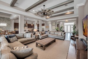 A spacious living room with a large sectional sofa, a wooden coffee table, and a dining area with a chandelier.