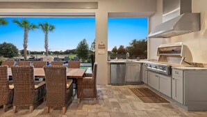 Cocina exterior con comedor, con sillas de mimbre y una mesa, y vista a palmeras y una piscina.