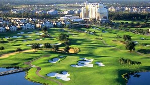 Un campo de golf con búnkeres, una masa de agua y un gran hotel al fondo.
