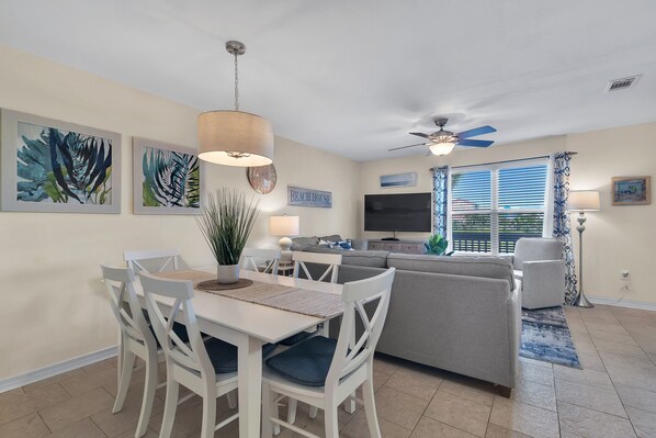 A dining area with a white table and chairs, a ceiling fan, and artwork on the walls.