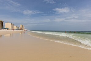 A beach with a sandy shore, waves, and buildings in the background.