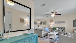 Un salon avec une commode vert turquoise, un canapé gris et un ventilateur de plafond.