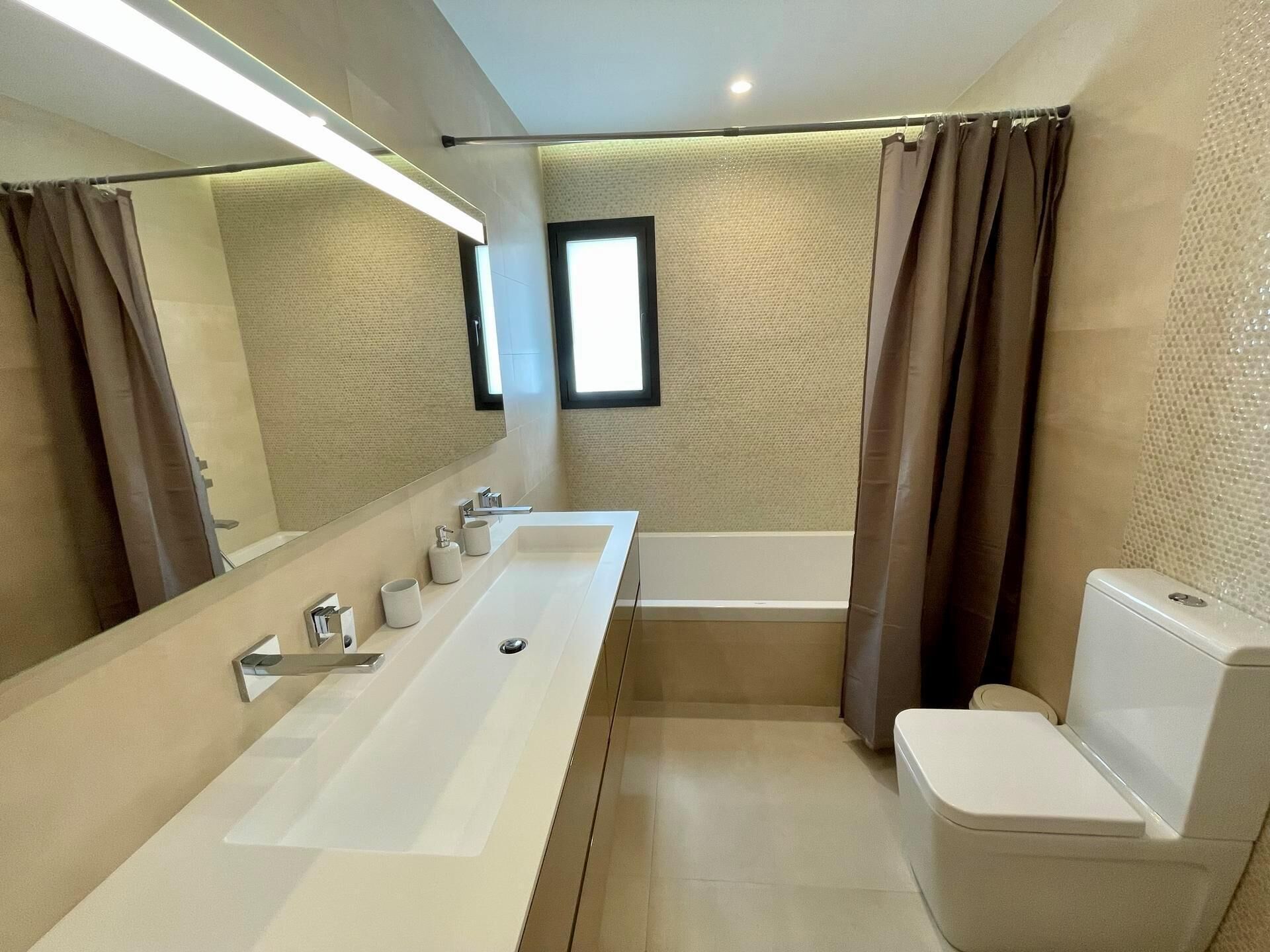 Un bagno moderno con un lavabo bianco allungato, una vasca da bagno e un water.
