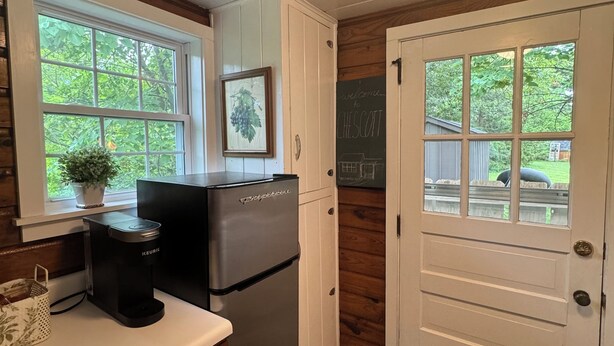 A kitchen with a refrigerator, a coffee maker, and a chalkboard with a welcome message.