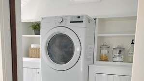A laundry area with stacked washing machines, a shelf with jars, and a window above.