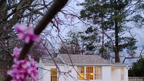 A white single-story house with a visible number '1507' on the side, a front yard with a sidewalk, and a tree with pink blossoms in the foreground.