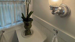 A bathroom with a white sink, a potted orchid, a white towel, and a wall-mounted light fixture.