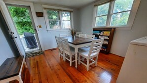 Una cocina con suelo de madera, armarios blancos, un refrigerador y una mesa de comedor con sillas.