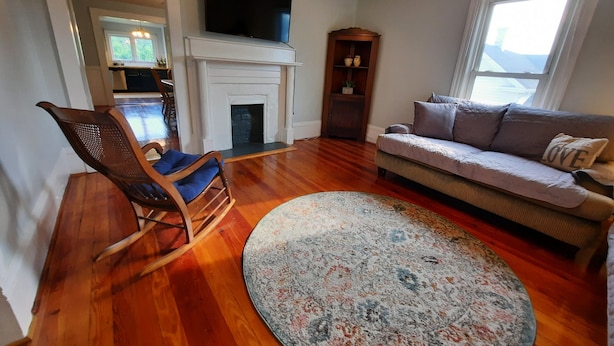 Una sala de estar con chimenea, un sofá, un sillón mecedor y un televisor montado en la pared.