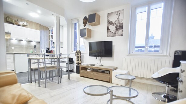 A modern living room with a kitchen area, a flat-screen TV, and a dining table with chairs.