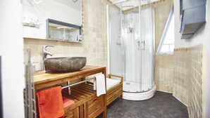 A bathroom with a stone basin sink, a wooden vanity, a towel rack, and a glass-enclosed shower.