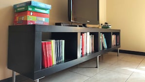 A black entertainment unit with a flat-screen TV and a stack of colorful books. - Organic breakfast in the garden, Vesuvius view (Castellammare di Stabia)