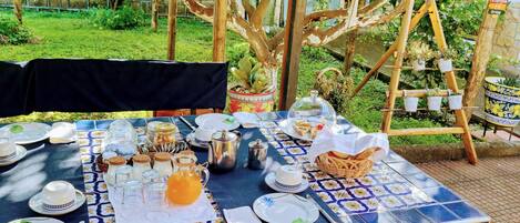 An outdoor dining area with a table set for a meal, surrounded by trees and a pergola.