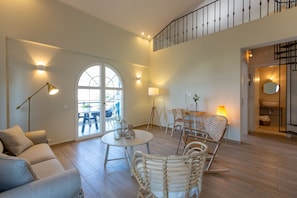 Ein geräumiges Wohnzimmer mit einer Couch, einem runden Tisch, Korbstühlen und einer Treppe zu einer oberen Ebene.