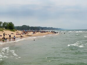 A crowded beach with people walking along the shore and others in the water.