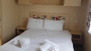 A neatly made bed with two rolled towels, wooden headboard with leaf patterns, and a small bedside table. - 2br-pool-garden-parking-wifi-sleeps6 (Paignton)