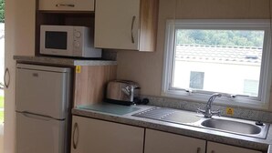 A compact kitchen with a built-in microwave, a toaster, and a sink under a window. - 2br-pool-garden-parking-wifi-sleeps6 (Paignton)