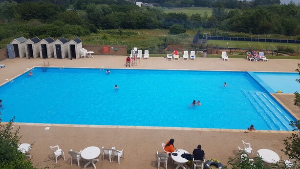 A swimming pool with multiple lanes, surrounded by lounge chairs and tables, with a view of a residential area in the background. - 2br-pool-garden-parking-wifi-sleeps6 (Paignton)