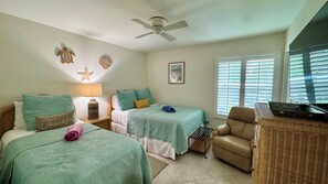A room with two beds, a ceiling fan, a window with blinds, a television, and a wicker chair. - Essex 106N: 5 Min walk to Beach, Movies, Restaurants (Marco Island)