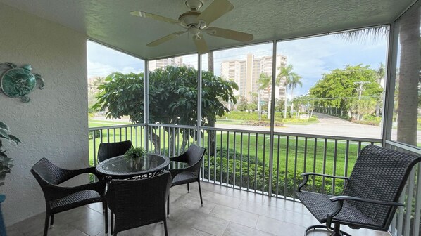Un balcon doté d’un ventilateur de plafond, d’une table ronde en verre et de quatre chaises en osier.