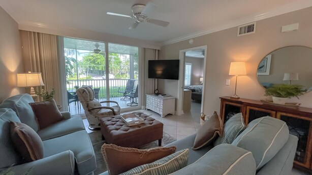 A spacious living room with a large sofa set, a television, and a ceiling fan. - Essex 106N: 5 Min walk to Beach, Movies, Restaurants (Marco Island)