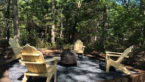 Zona boscosa con tres sillas Adirondack de madera dispuestas alrededor de un brasero.