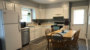 Una cocina con armarios blancos, un refrigerador, una estufa y una mesa de comedor con sillas.