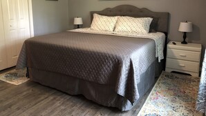 Un dormitorio con una cama grande, dos mesitas de noche, una puerta y un cuadro en la pared.