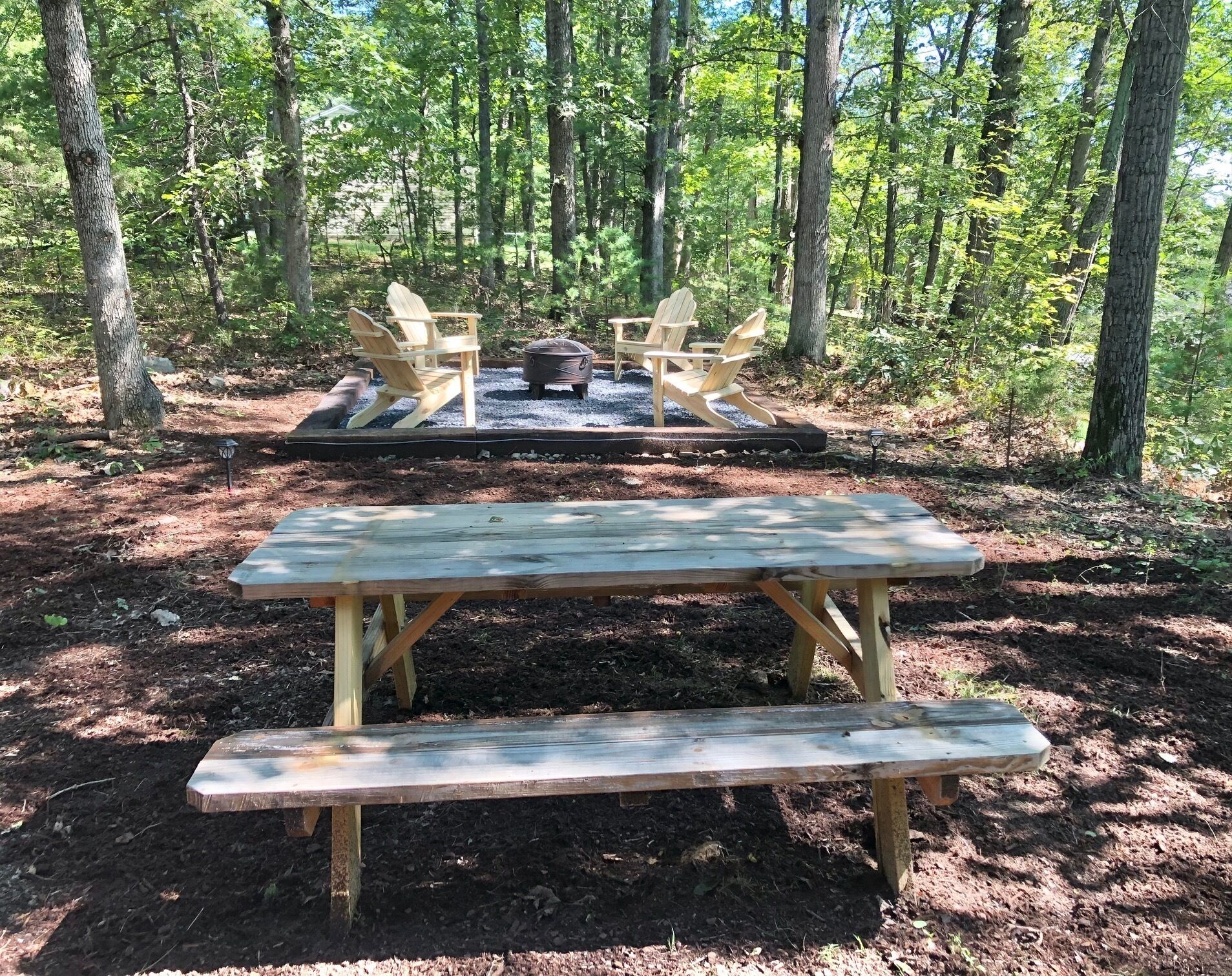 Un área de picnic con una mesa y bancos de madera, rodeada de árboles.
