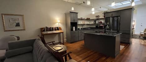 A modern kitchen with a central island, wooden flooring, and pendant lighting.