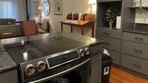 A modern kitchen with a built-in stove, a dining area with a table and chairs, and a living room with a sofa and a lamp. - Palafox Loft 122, sleeps 2 (Pensacola)