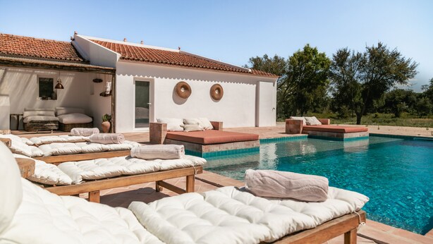 Un espace aménagé au bord de la piscine, avec des chaises longues et un petit bâtiment doté d’un toit en tuiles.