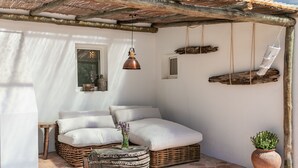 Une pièce chaleureuse avec un canapé en osier, une petite table ronde, un luminaire suspendu et une plante en pot.