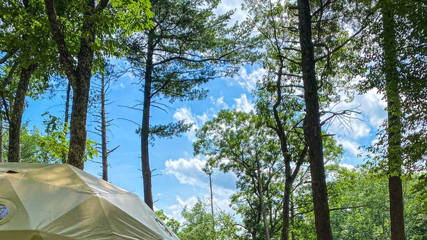 A dome-shaped tent with a wooden deck and red chairs, surrounded by trees in a forest. - Cozy, Seasonal Geo-Dome with Heat/AC on Private Hiking paradise in Gunks. (Wallkill)