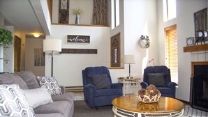Ein Wohnzimmer mit grauem Sofa, zwei blauen Sesseln, einem Holztisch und einem Kamin.