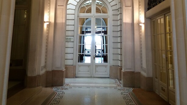 Un vaste hall d’entrée avec une grande porte en arc de cercle, un lustre et un sol à motifs.