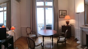 Une pièce avec un plancher en bois, une table à manger entourée de quatre chaises, une cheminée et un grand miroir.