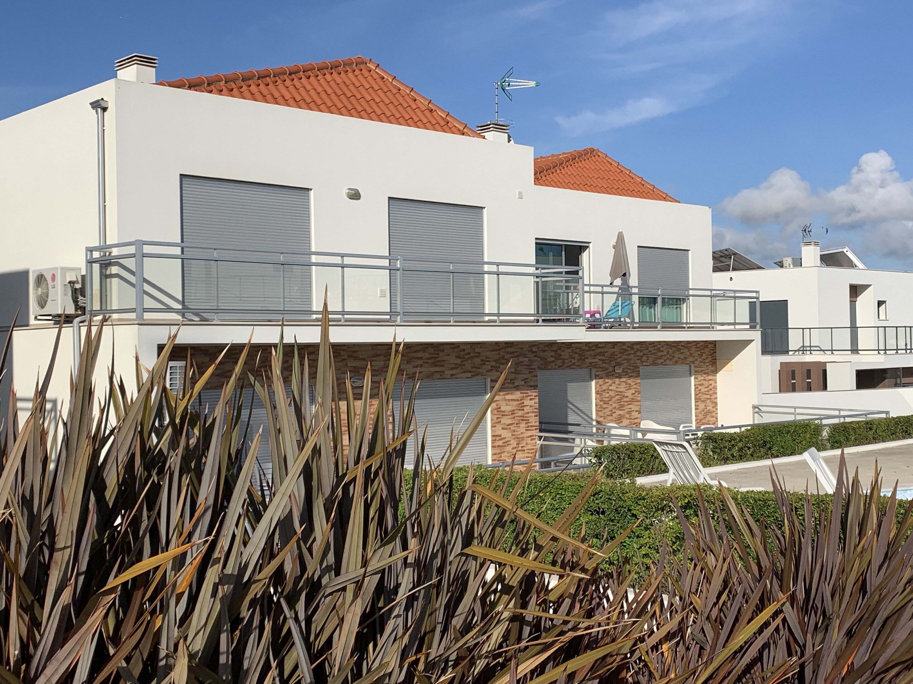A modern two-story building with a red-tiled roof, large garage doors, and a balcony with a metal railing.