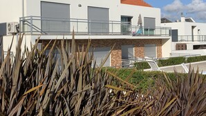 Un edificio moderno a due piani con tetto in tegole rosse, ampie porte per garage e un balcone con ringhiera in metallo.