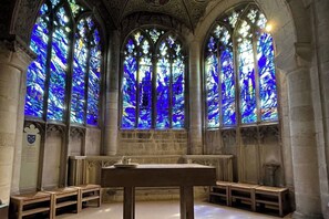 A church interior with three large stained glass windows, a wooden altar, and stone columns. - Casita Lodge | Hot tub Stay for two in the Forest of Dean (Cinderford)