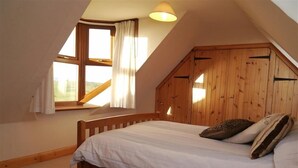 A bedroom with a sloped ceiling, wooden bed frame, and a window with curtains. - Allanhead Cottage -  a cottage that sleeps 8 guests  in 3 bedrooms (Kirkcudbright)