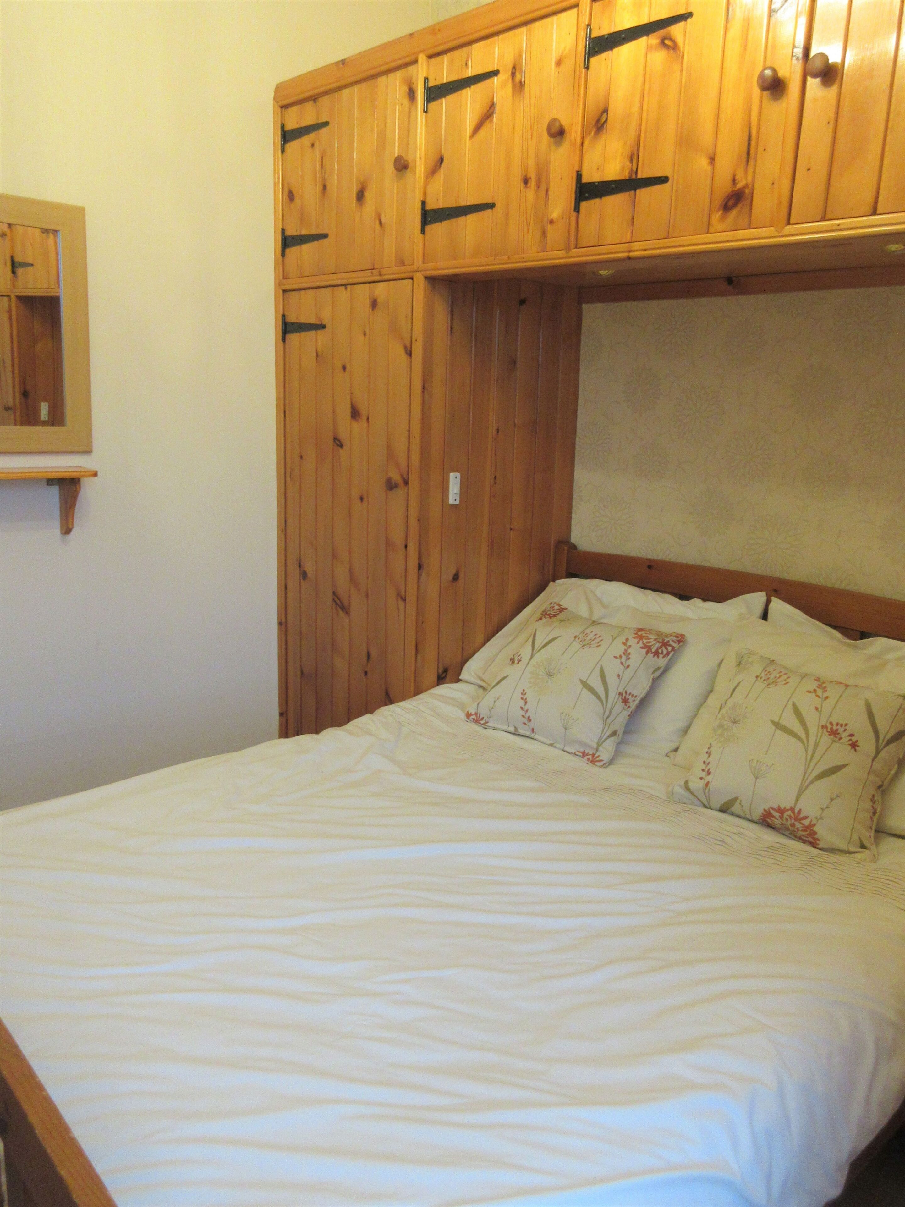 A bedroom with a wooden headboard, a bed with floral bedding, and a small shelf above the bed.