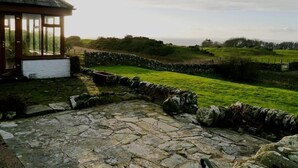 A stone pathway leading to a wooden structure with a view of a grassy field and stone wall. - Allanhead Cottage -  a cottage that sleeps 8 guests  in 3 bedrooms (Kirkcudbright)